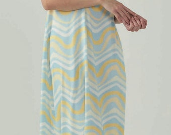 Könnte beinhalten: Ein hellblaues Maxikleid mit einem wellenförmigen Muster in Gelb und Weiß. Das Kleid hat einen Halterneck mit einem türkisfarbenen Quastenband.