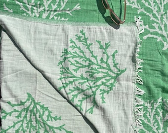 May include: A green and white beach towel with a coral reef design. The towel is folded in half and has a fringe border.