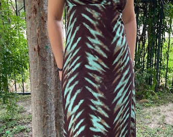 May include: A long, brown and teal maxi dress with a chevron pattern. The dress has a V-neckline and short, ruffled sleeves. The model is wearing a turquoise pendant necklace.