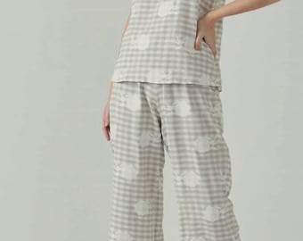 May include: A beige and white gingham pajama set with a floral print. The top has a V-neck and a tassel tie. The pants are wide-legged.