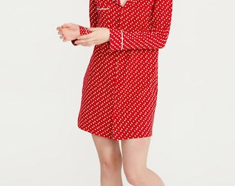 May include: A red and white polka dot sleep shirt with long sleeves and a collared neckline. The shirt has white piping around the collar and cuffs.