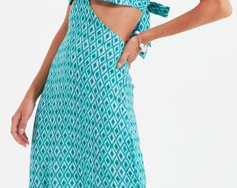 May include: A turquoise blue maxi dress with a diamond pattern. The dress has a cut-out detail at the waist and a tie at the back. The dress has a side slit.