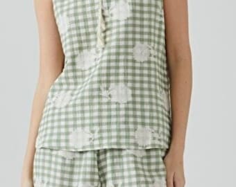 May include: A green and white gingham pajama set with white embroidered flowers. The top has a V-neck and a tie at the neckline. The shorts have a relaxed fit.