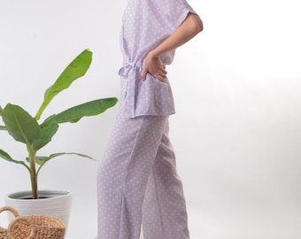 May include: A lavender pajama set with a white polka dot pattern. The top has a wrap style and a tie at the waist. The pants are wide-legged.