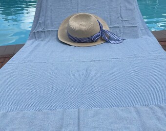 May include: A light blue beach towel with a white and blue checkered pattern. A straw hat with a blue and white checkered ribbon is on top of the towel.