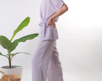 May include: A lilac pajama set with a white polka dot pattern. The top has a wrap style and a tie at the waist. The pants are wide-legged.