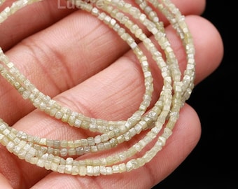May include: A strand of light green diamond beads, each bead is square shaped and faceted. The beads are strung on a thin wire and are displayed on a hand.