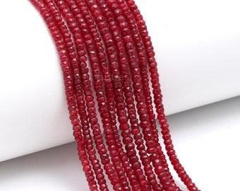 May include: A strand of red gemstone beads, faceted and round, strung on a white surface. The beads are small and uniform in size.