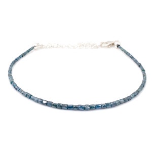 Puede incluir: Un delicado brazalete de cadena de plata con una fila de pequeñas piedras azules de forma cuadrada.