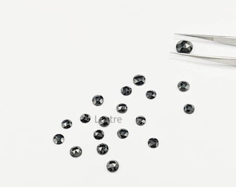 May include: A group of black faceted gemstones, some of which are being held by tweezers, on a white surface.