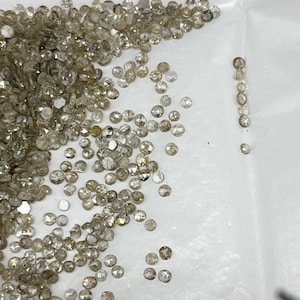 May include: A pile of small, round, light brown diamonds on a white surface. Some of the diamonds are arranged in a line.