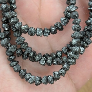 May include: A strand of black diamond beads, each bead is a rough, uncut diamond with a dark, metallic sheen.