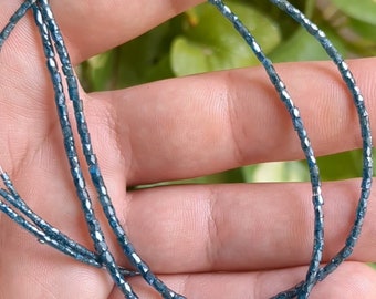 May include: A strand of blue faceted beads, likely made of glass or crystal, is shown in a close-up image. The beads are small and uniform in size, and they have a slightly iridescent sheen.