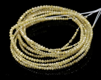 May include: A strand of light yellow diamond beads. The beads are small and faceted, giving them a sparkling appearance. The strand is coiled and laid out on a black surface.