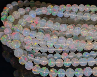 May include: A strand of iridescent white opal beads. The beads are round and have a translucent, milky appearance with flashes of colour.