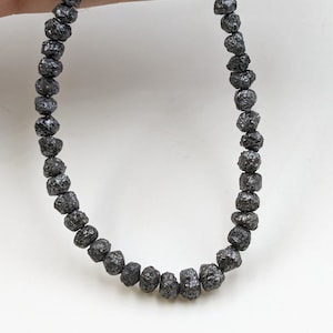 May include: A strand of black rough diamond beads. The beads are round and have a rough, textured surface.