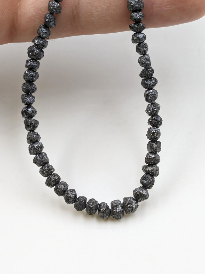 May include: A strand of black rough diamond beads. The beads are round and have a rough, textured surface.