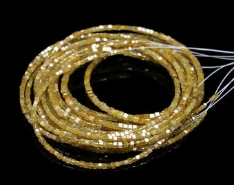 May include: A strand of yellow gemstone beads, each bead is a square shape. The beads are strung on a white thread and are arranged in a circular pattern.