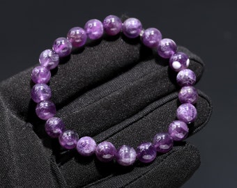 May include: A purple amethyst gemstone bracelet with a round bead design. The bracelet is made of natural stones and has a polished finish.