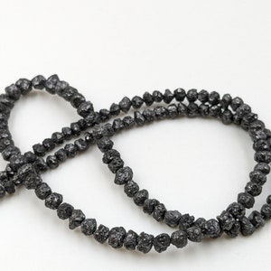 May include: A strand of black, rough, and irregularly shaped beads. The beads are made of black diamonds.