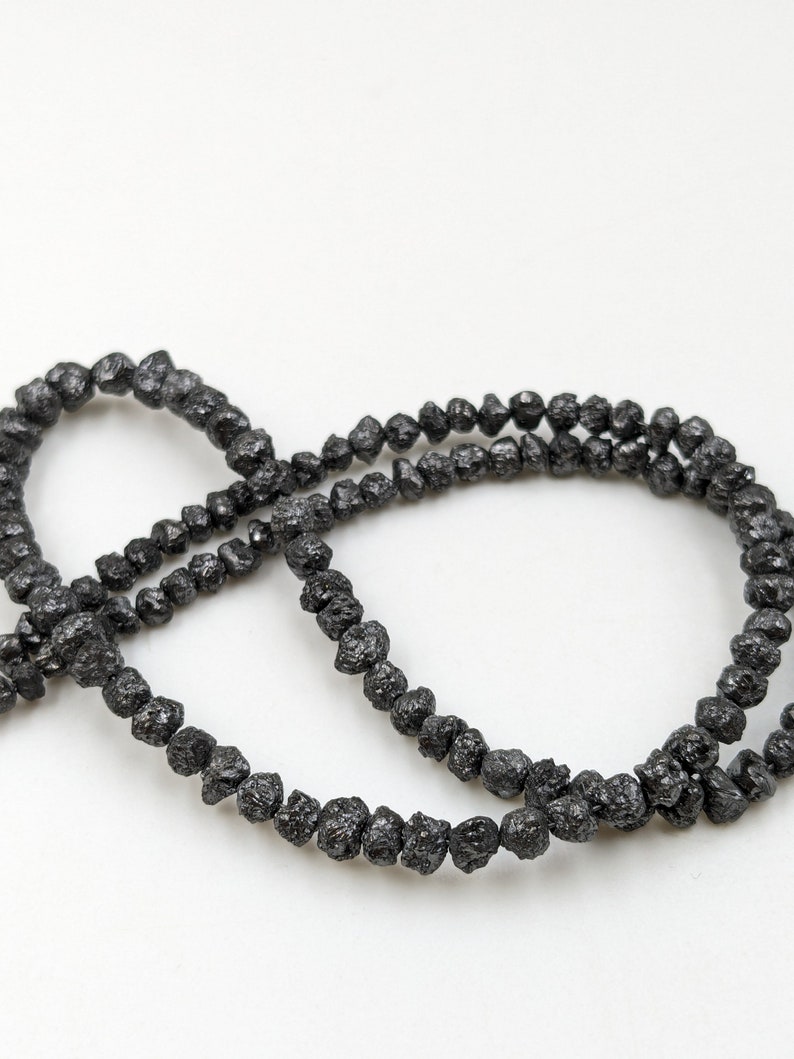May include: A strand of black, rough, and irregularly shaped beads. The beads are made of black diamonds.