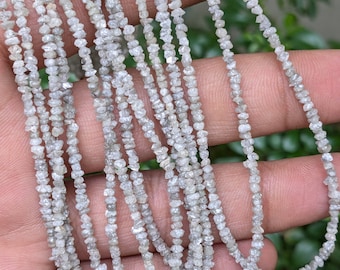 May include: A strand of rough, white diamond beads. The beads are small and irregular in shape, and they are strung together on a clear thread. The beads are arranged in a loose, flowing pattern.