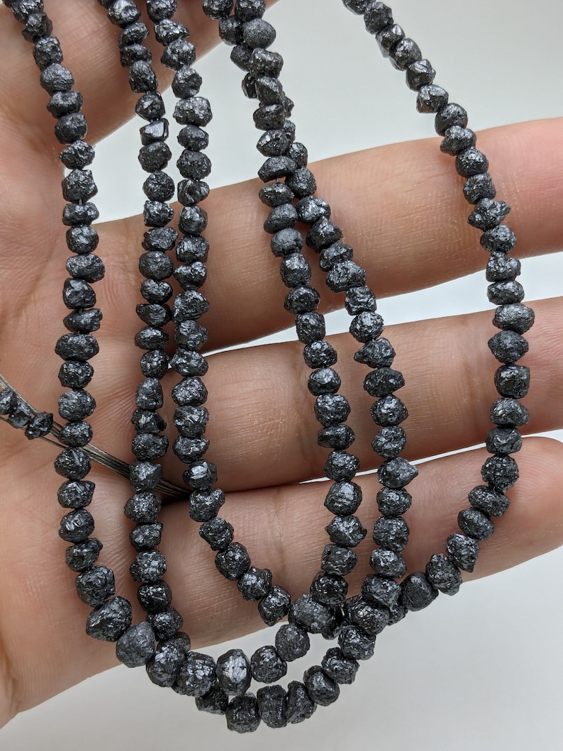 May include: A strand of black diamond beads, each bead is faceted and has a rough, natural texture. The beads are strung on a thin wire and are approximately 3mm in diameter.