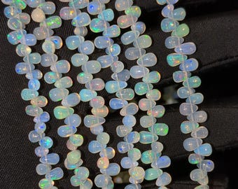 May include: A strand of white opal beads with iridescent rainbow colors. The beads are teardrop shaped and strung on a clear thread.