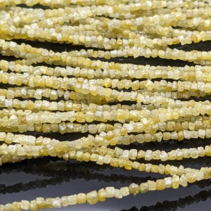May include: Close-up of strands of rough-cut, light yellow diamonds. The gemstones are small, with irregular shapes, and are strung together. The overall effect is a shimmering, textured surface, ideal for jewelry making.