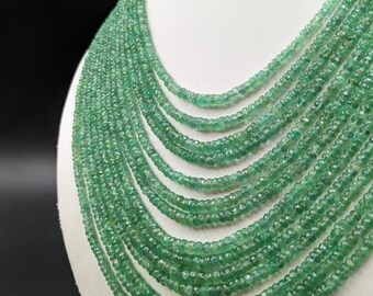 Pode incluir: Um fio de contas de pedras preciosas verde esmeralda, enfiadas para formar um colar. As contas são facetadas e têm uma forma ligeiramente irregular.