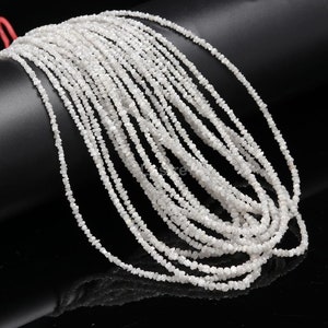 May include: A strand of white rough diamond beads. The beads are small and irregular in shape, and they are strung together on a clear thread. The beads are arranged in a loose, flowing pattern.