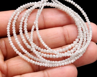 May include: A strand of white diamond beads, each bead is faceted and has a rough, natural look. The beads are strung on a white thread and are arranged in a circular shape.