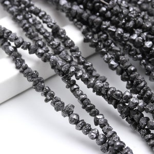 Puede incluir: Una hebra de cuentas de diamante negro en bruto. Las cuentas son de forma irregular y tienen un acabado mate.