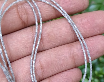 May include: A strand of silver-toned beads, made of faceted, square-shaped beads. The beads are strung on a clear thread and are arranged in a circular shape.