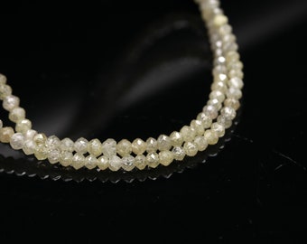 May include: A double strand necklace made of small, faceted, light yellow diamonds. The diamonds are strung on a thin wire and the necklace is lying on a black surface.