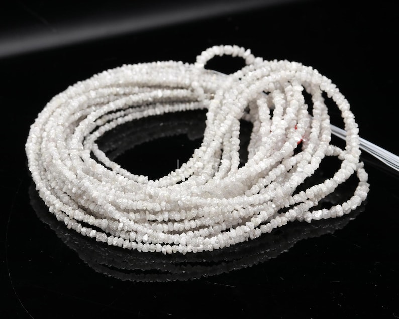 May include: A strand of white rough diamonds, also known as uncut diamonds, strung together on a white thread. The diamonds are small and have a natural, unpolished look.
