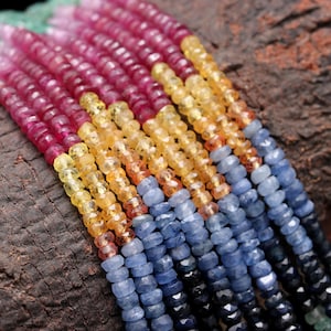 Può includere: Un filo di perline di pietre preziose colorate, tra cui perline rosse, gialle e blu. Le perline sono sfaccettate e hanno una finitura liscia e lucida.