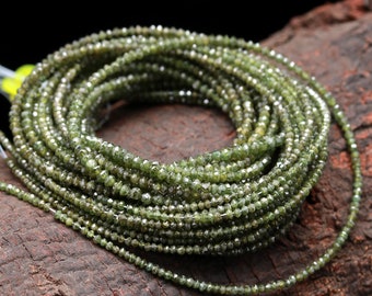 May include: A strand of green faceted gemstone beads. The beads are small and round, and they are strung on a thin wire. The beads are arranged in a circular pattern, and they are lying on a piece of wood.