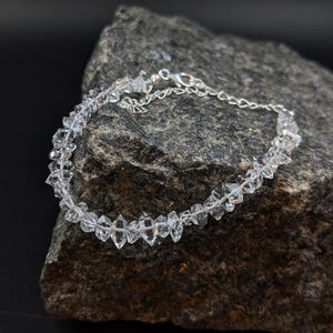 Peut inclure: Un bracelet en argent avec des perles de cristal facettées transparentes. Le bracelet est sur un rocher gris.