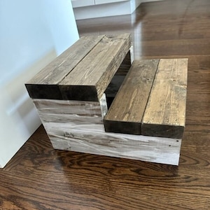 May include: A two-step wooden stool with a natural wood stain and white paint. The stool has a rustic look and is made of solid wood.