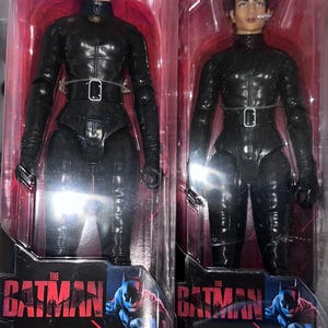Peut inclure: Deux figurines articulées identiques de Selina Kyle tirées de The Batman, chacune dans son emballage plastique transparent d'origine. Les figurines ont les cheveux courts et portent une combinaison noire texturée avec une ceinture. Le logo DC est visible.