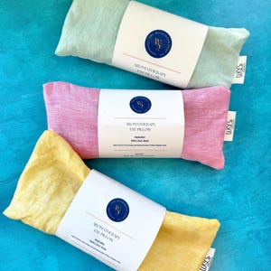 May include: Three aromatherapy eye pillows, one green, one pink, and one yellow, with white labels that say "Aromatherapy Eye Pillow" and "Handcrafted".
