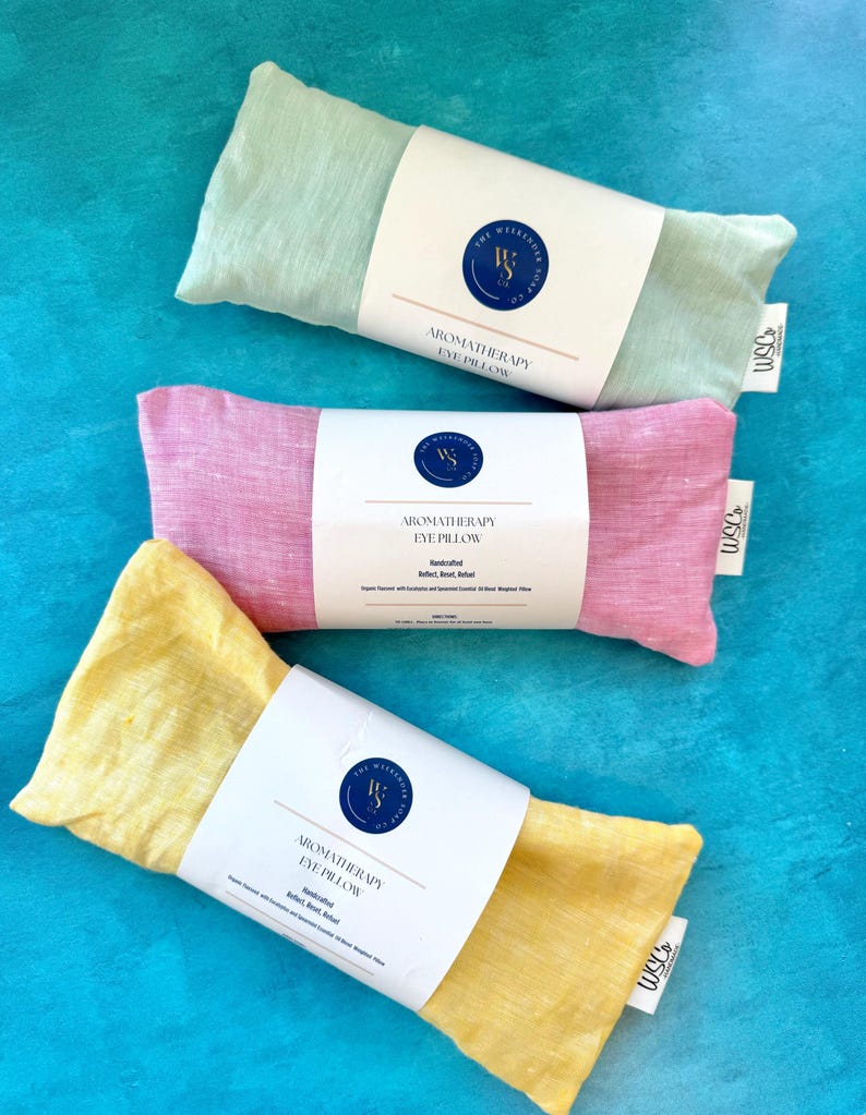May include: Three aromatherapy eye pillows, one green, one pink, and one yellow, with white labels that say "Aromatherapy Eye Pillow" and "Handcrafted".