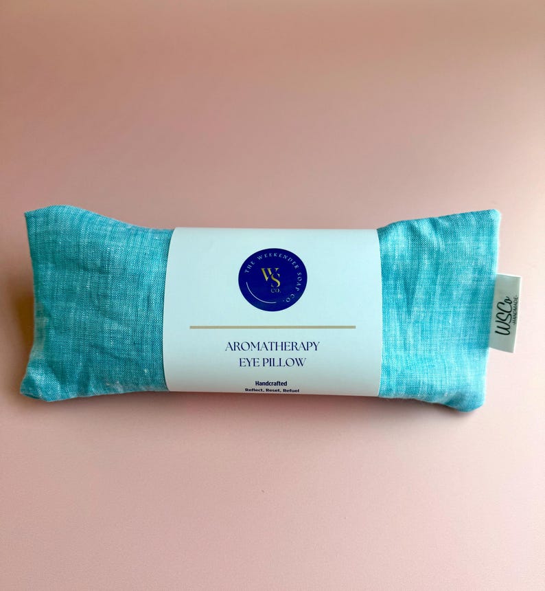 May include: A teal blue aromatherapy eye pillow with a white label that reads "The Weekend Soul Co." and "Aromatherapy Eye Pillow" with the text "Handcrafted" below.