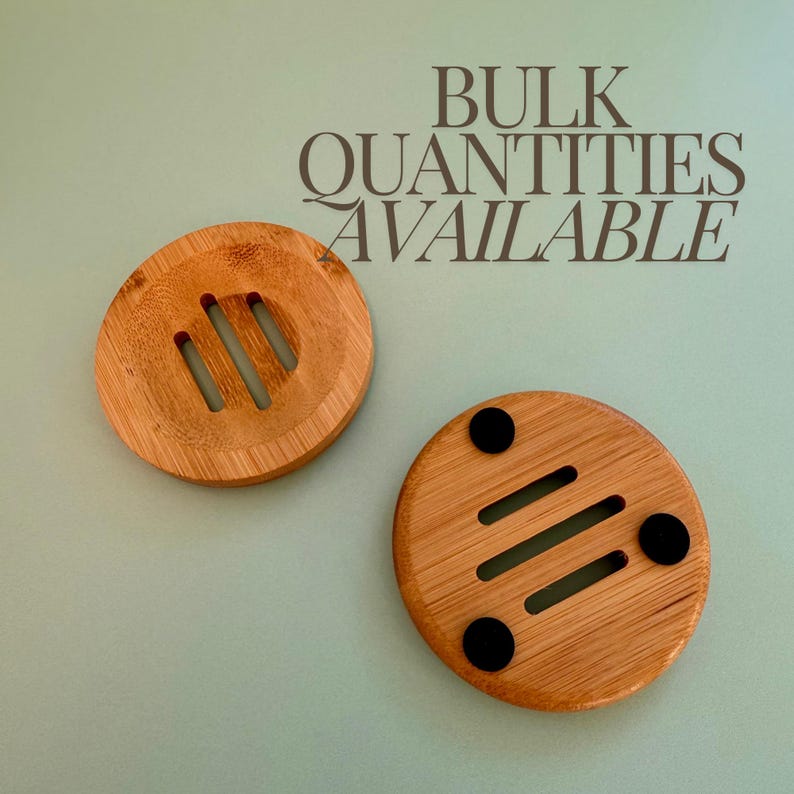 May include: Two round wooden soap dishes with drainage slots. The dish on the left has a natural wood finish. The dish on the right has a natural wood finish with three black rubber feet on the bottom. The text "BULK QUANTITIES AVAILABLE" is visible in the top center of the image.