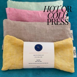 May include: Four linen eye pillows in different colors: green, pink, beige, and yellow. The yellow pillow has a white label that reads "Aromatherapy Eye Pillow, Handcrafted, Reflect, Boost, Refill, Organic flaxseed with lavender and geranium essential oil blend weighted pillow". The text "Hot or Cold Press" is written in black on a white background.