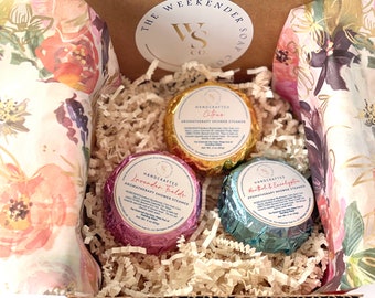 May include: A gift box filled with three aromatherapy shower steamers. The steamers are wrapped in foil and labeled with the scents "Citrus", "Lavender Fields", and "Menthol & Eucalyptus".