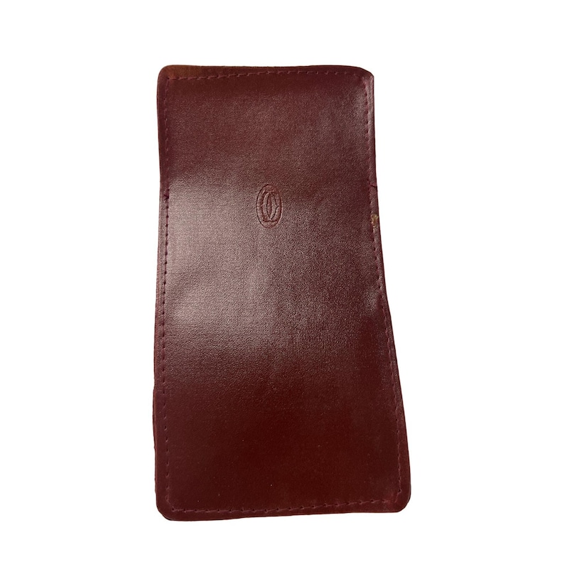 May include: A burgundy leather Cartier card holder. The card holder is a rich, dark red color and has a subtle, embossed Cartier logo.  The stitching is visible around the edges. It appears to be made of high-quality leather, suitable for holding cards or other small items. The compact size suggests it is designed for portability and convenience.