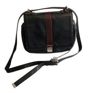 May include: Black leather crossbody bag with a brown vertical stripe and silver hardware. The bag has a flap closure, a long adjustable strap, and a chain detail on the side. The bag has two front pockets and a top handle.