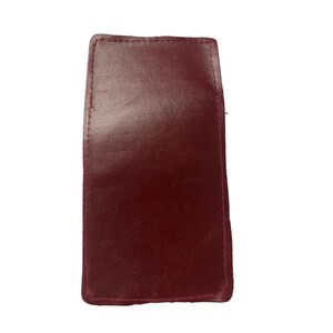 May include: A burgundy-colored leatherette wallet. The wallet is rectangular with slightly rounded corners and features a smooth, matte finish.  The stitching along the edges is visible. The material appears to be a synthetic leather, offering a sleek and compact design suitable for everyday use. This simple yet elegant wallet is ideal for carrying cards and cash.